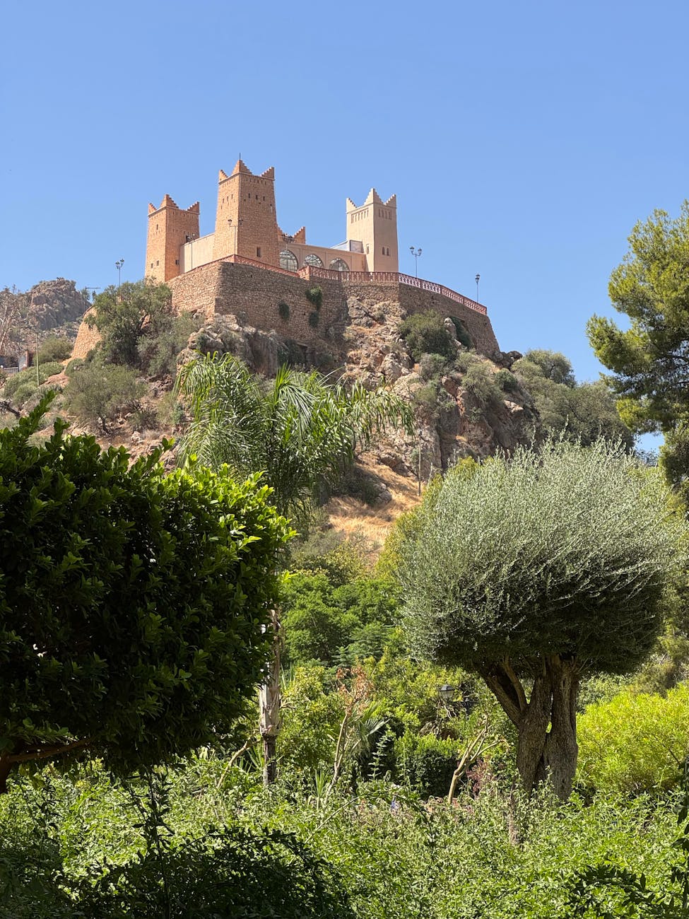 Une vue imprenable sur le château historique de Beni Mellal perché sur une colline entourée d'une verdure luxuriante sous un ciel bleu clair.
