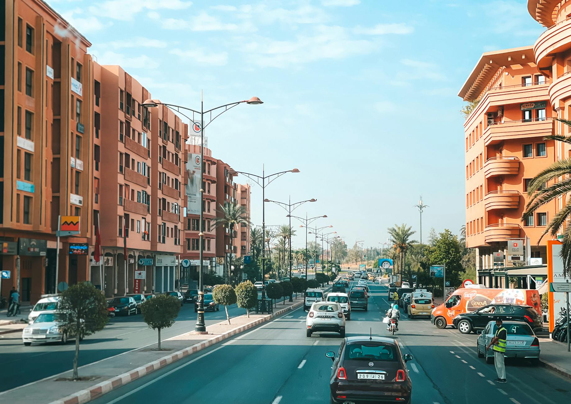 Scène de rue animée à Marrakech avec circulation et architecture distinctive sous un ciel bleu vif.