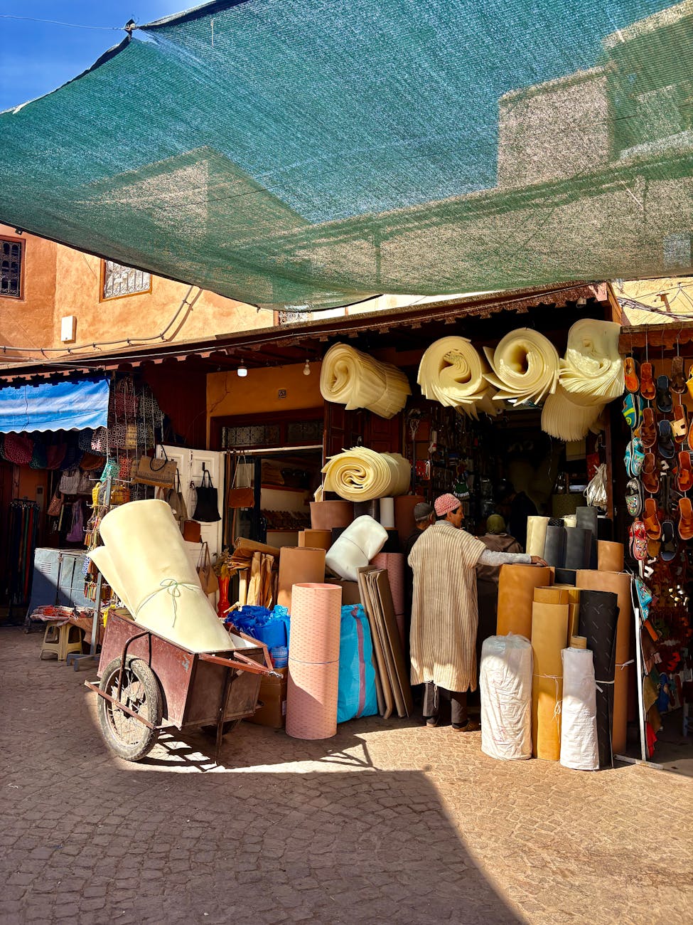 Boutique colorée du souk de Marrakech, proposant divers articles et textiles sous une verrière ensoleillée.