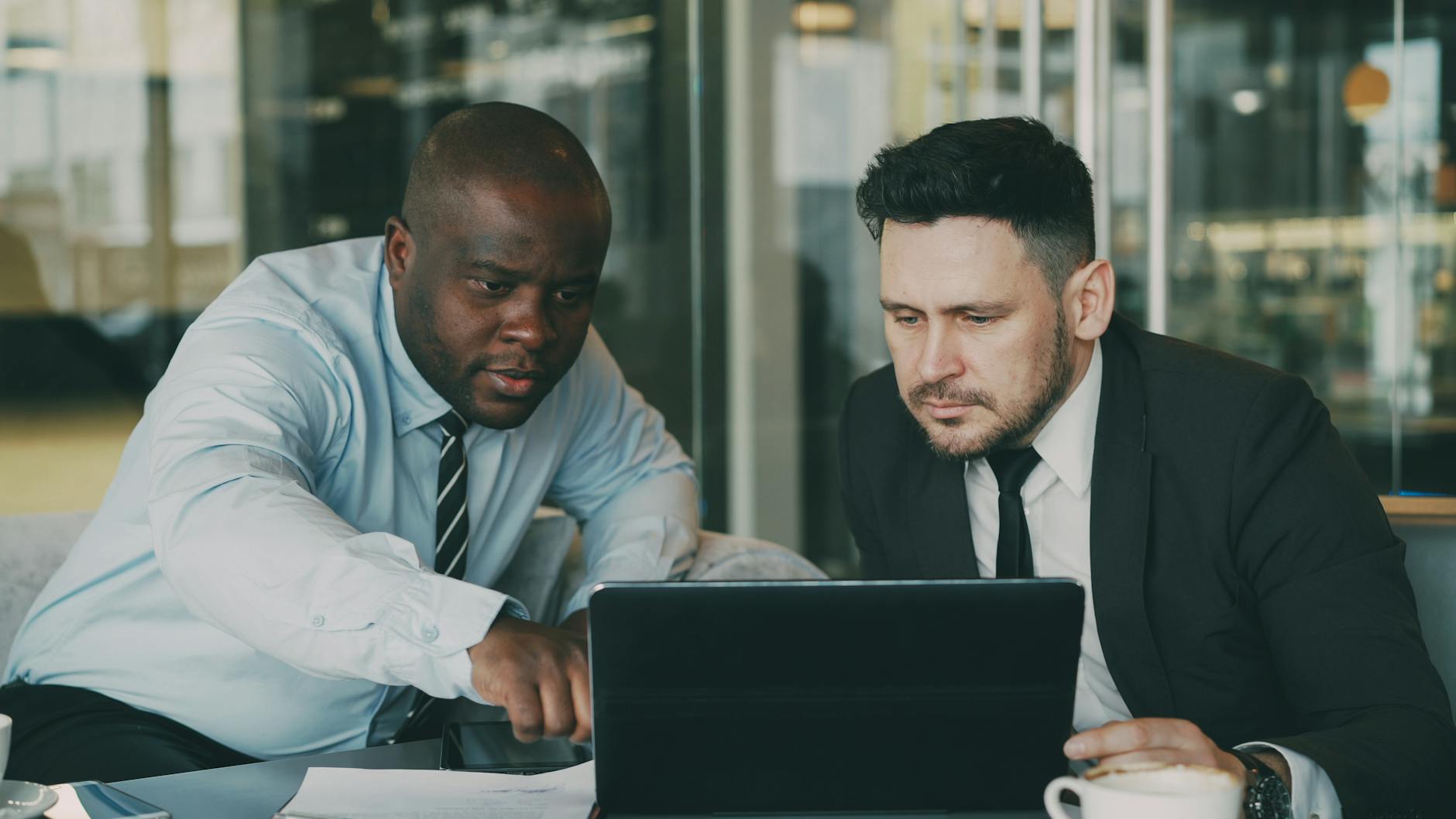Deux hommes d'affaires concentrés sur une tablette, collaborant dans un environnement de bureau moderne.