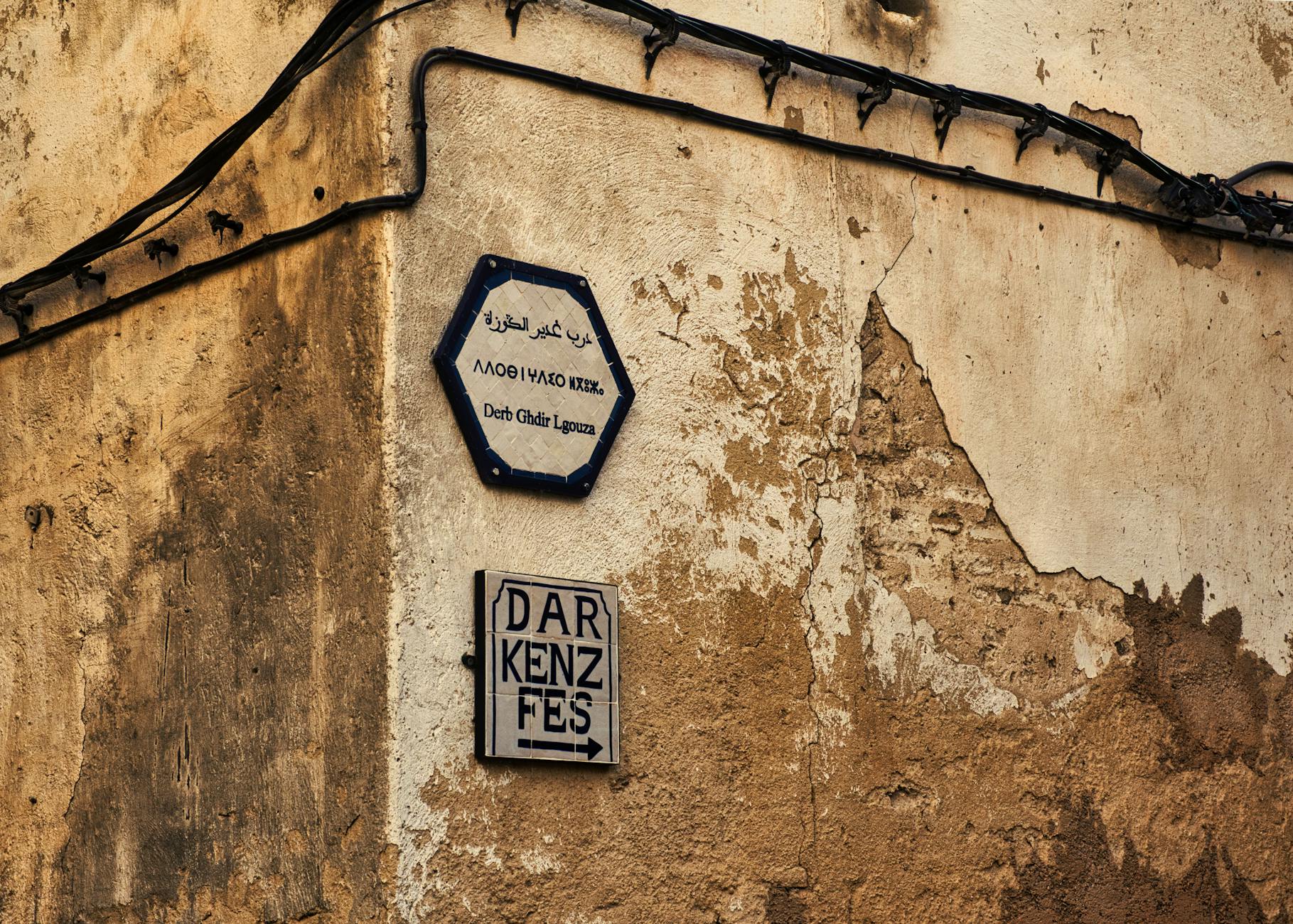 Panneaux de signalisation sur un mur rustique de la médina de Fès, au Maroc, mettant en valeur le patrimoine culturel.